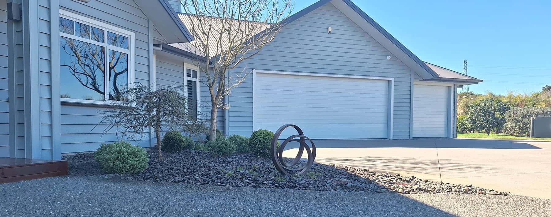 Pebble garden with clipped shrubs, maples and a ring sculpture at a home entrance