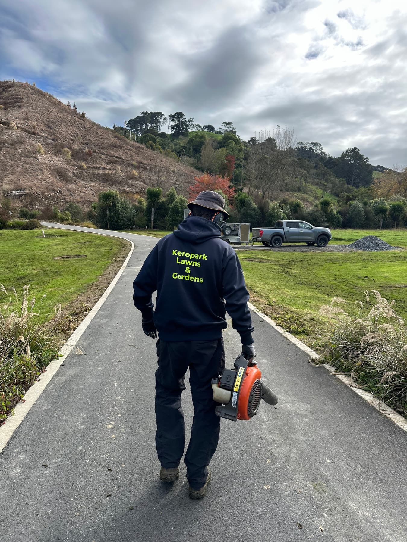Team member in KLG hoodie walking rural drive with blower
